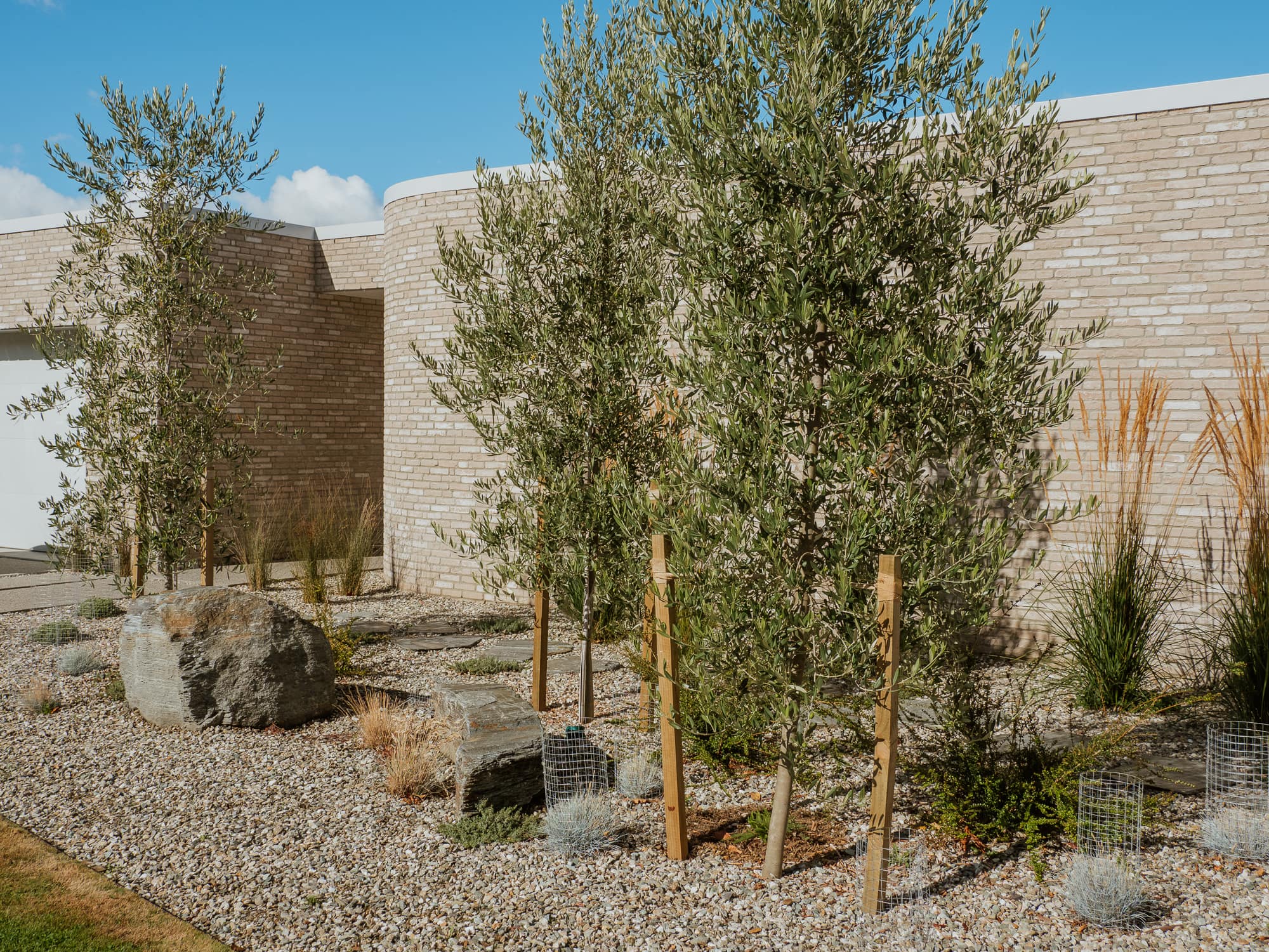 Pale brick home with curved walls, olive trees and schist boulders