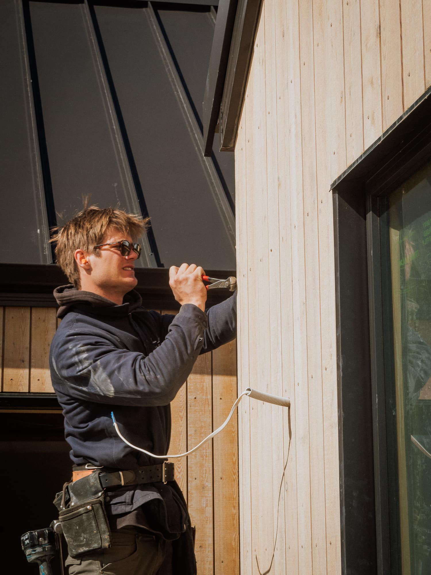 A builder fixing cedar cladding beneath a black steel roof at Jack's Point