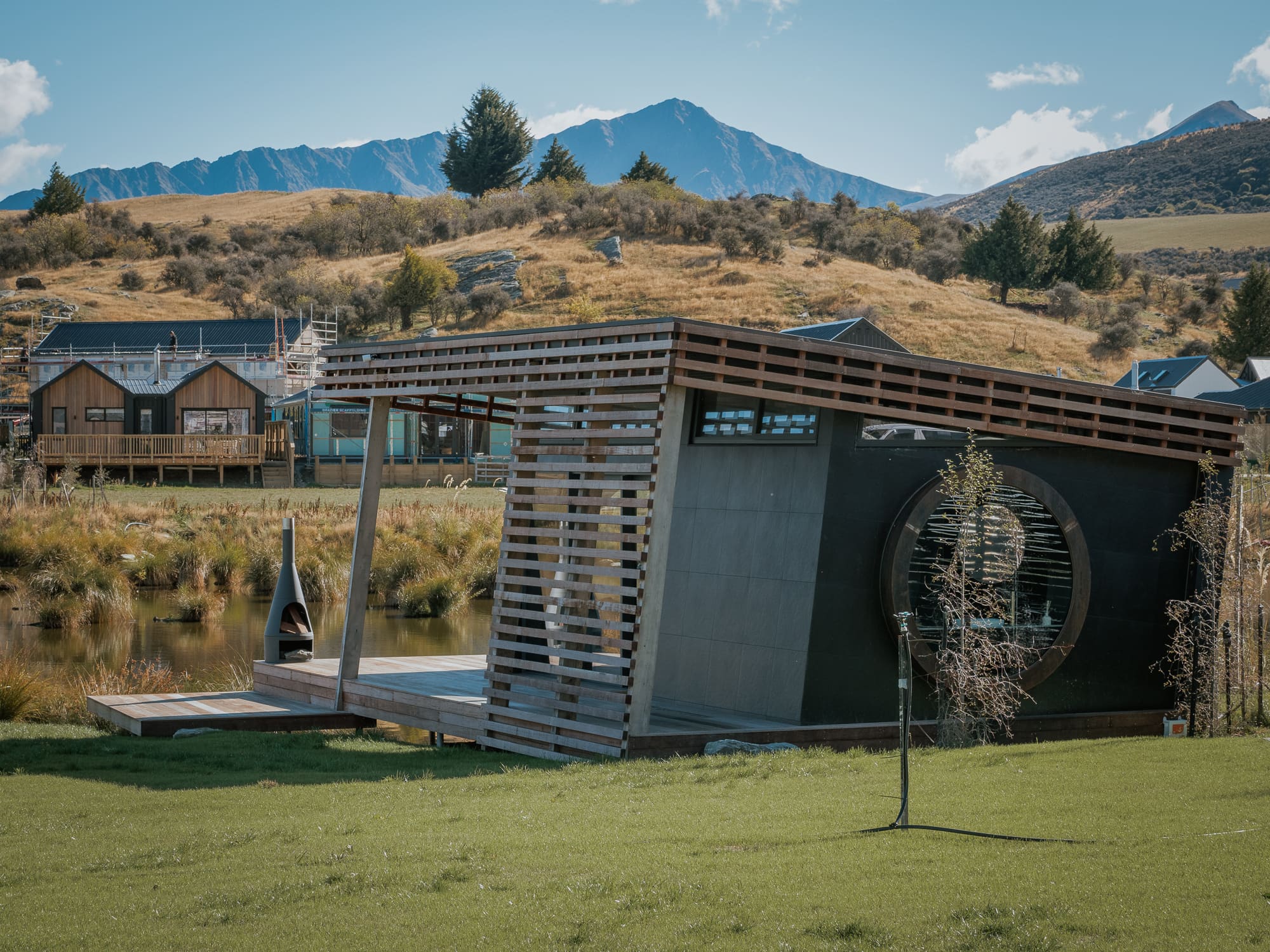 A black cedar pavilion beside a pond in the Wakatipu Basin, mountains behind