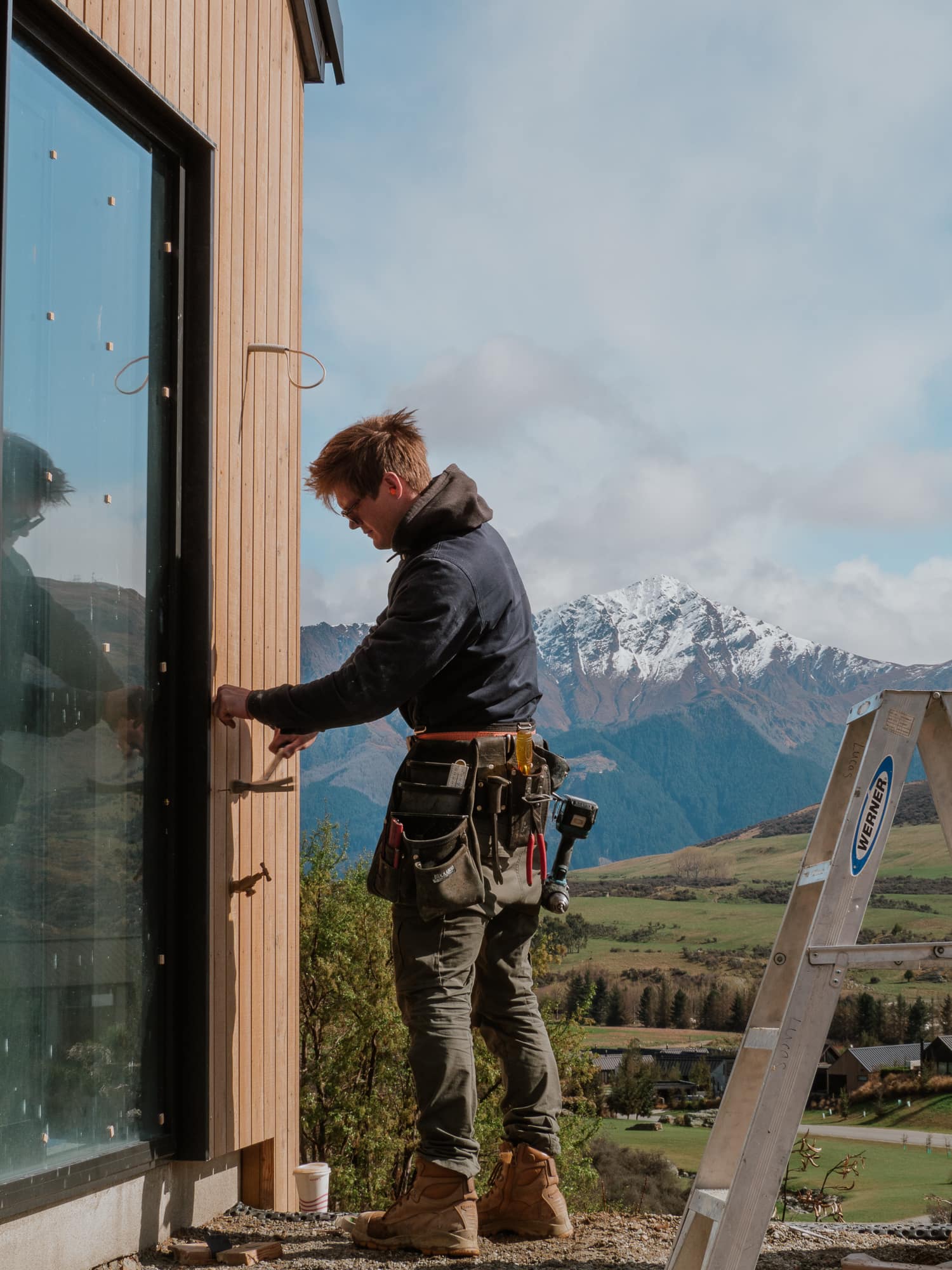 A builder fixing cedar cladding beneath the mountian peaks